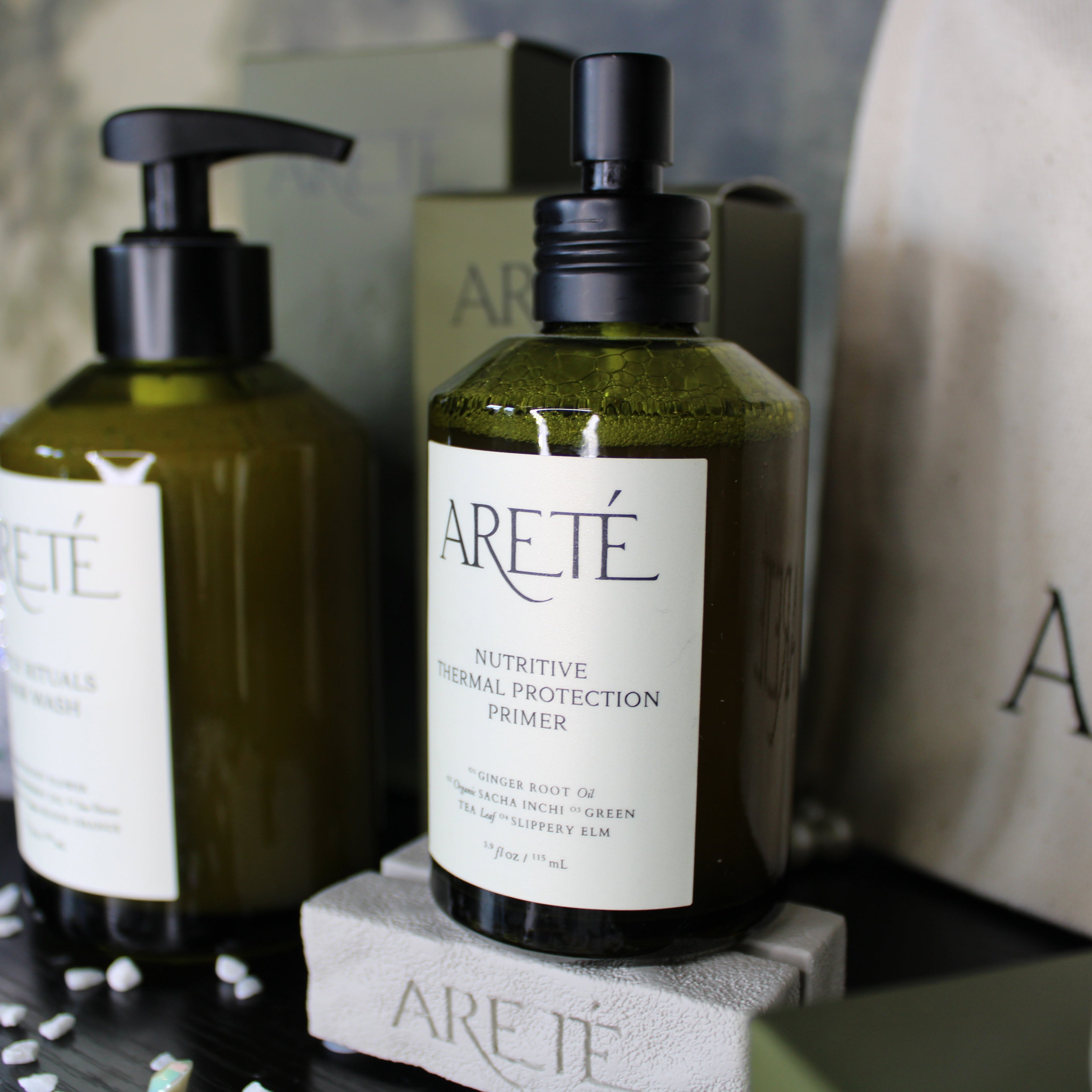 Two bottles of Arete skincare products on a dark surface with a branded bag in the background.