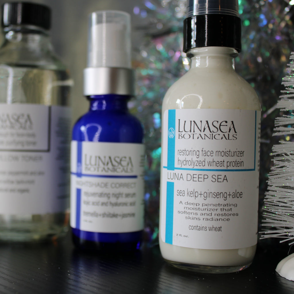 Collection of Lunasea Botanics skincare products on a dark surface with a blurred decorative background.