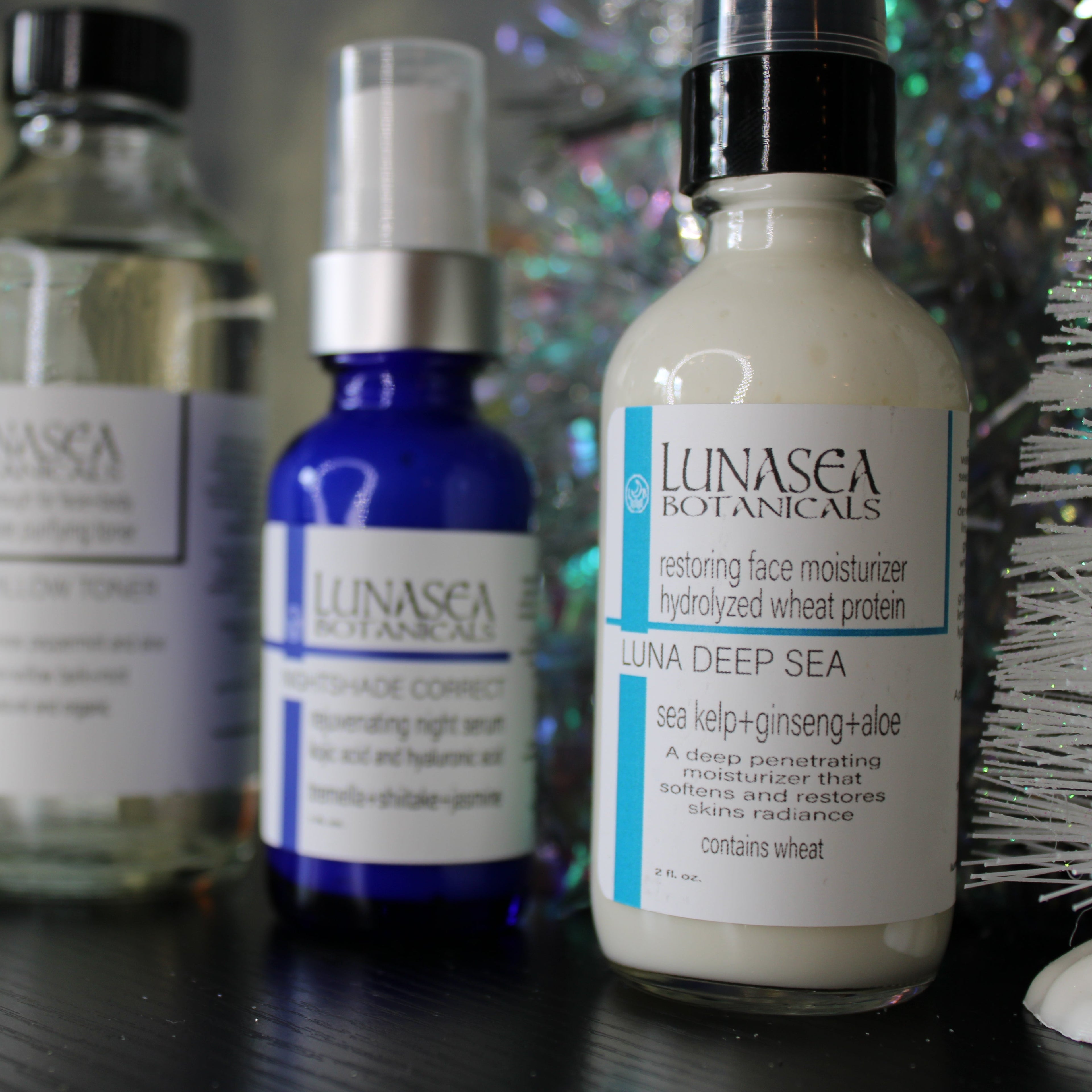 Collection of Lunasea Botanics skincare products on a dark surface with a blurred decorative background.