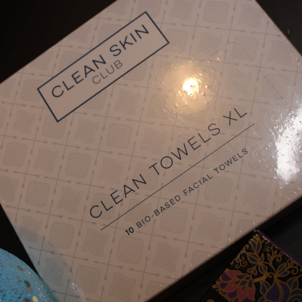 Box of Clean Skin Club Clean Towels XL on a dark surface with decorative items around.