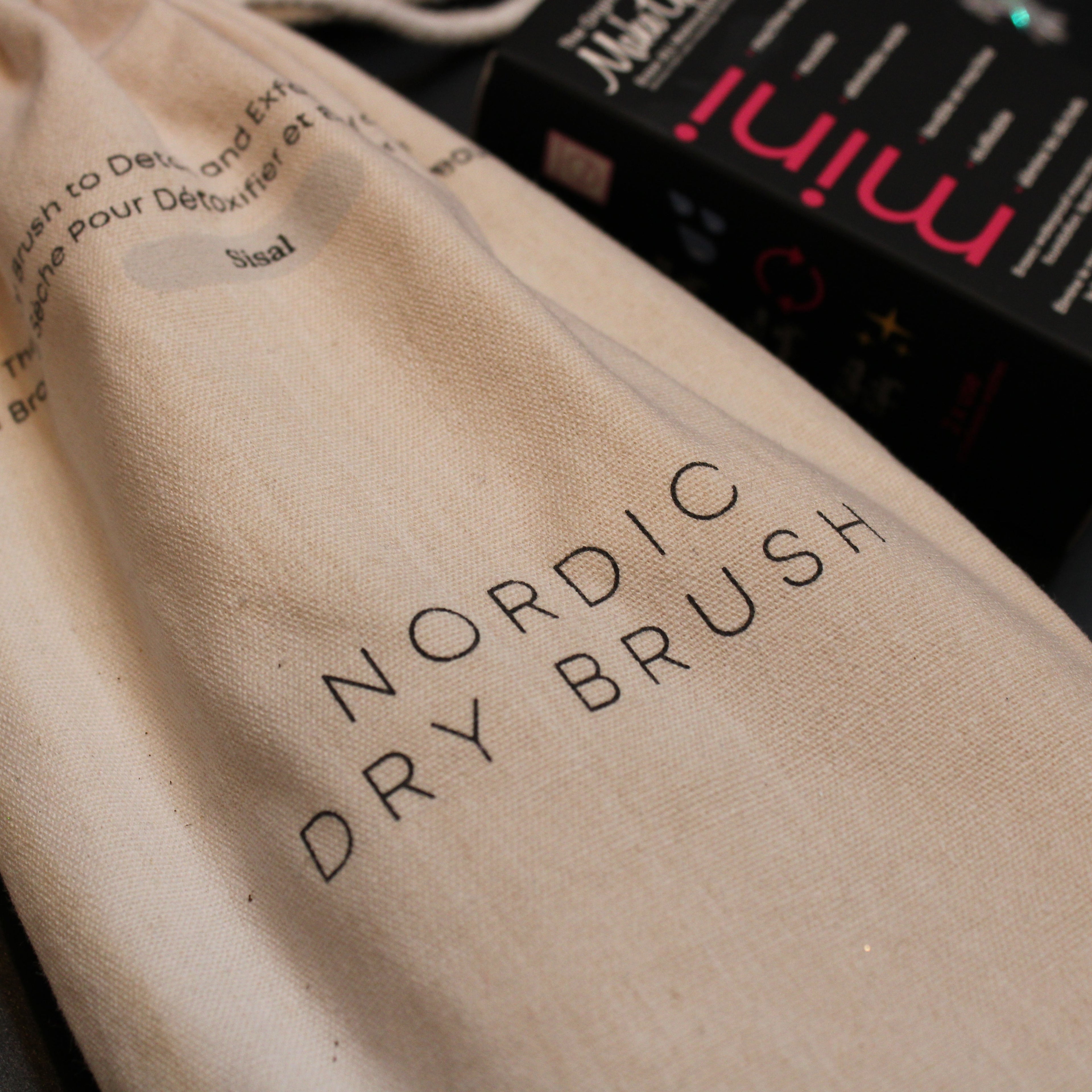 Beige drawstring bag with 'Nordic Dry Brush' text on a dark surface with a product box in the background.