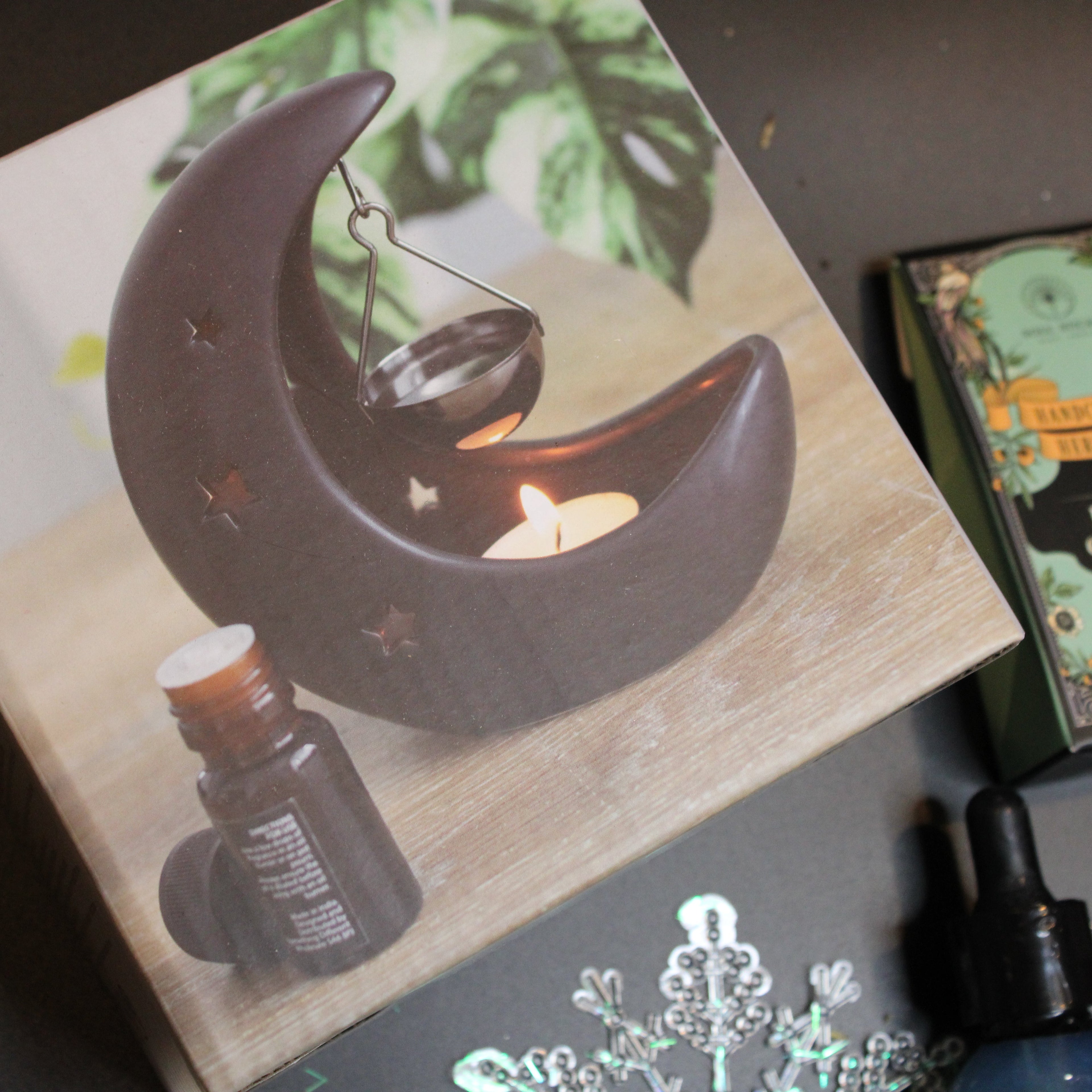 Crescent moon-shaped candle holder with a lit candle on a book, surrounded by other items.