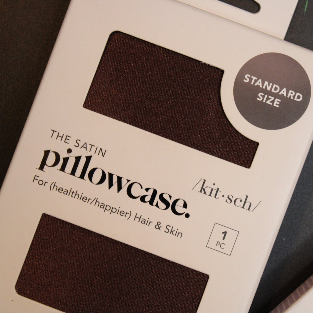 Packaged satin pillowcase with branding and product details on a dark surface.