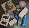 Collection of items including candles, bottles, and packaging on a dark surface with decorative elements.
