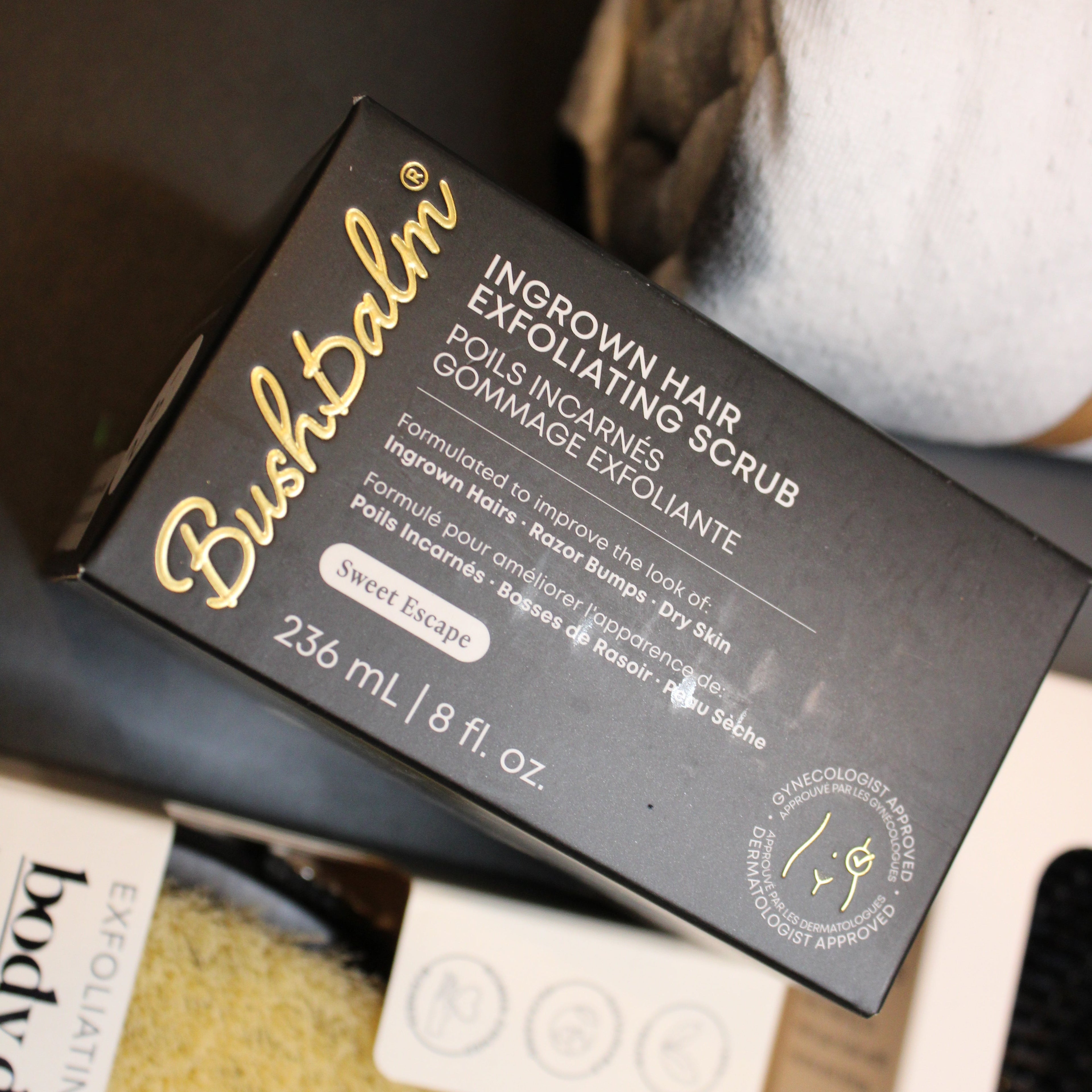 Box of Body Drench ingrown hair scrub with a brush and towel in the background