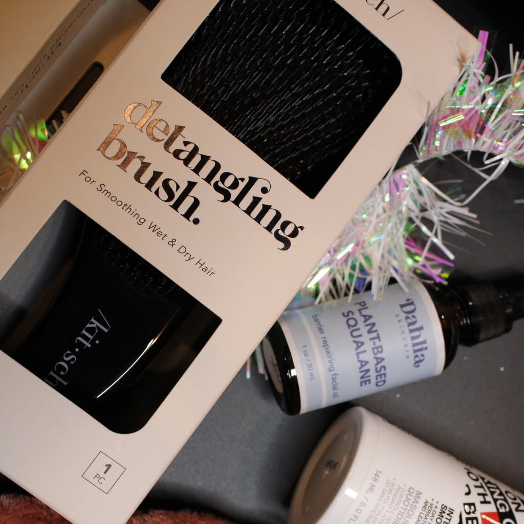 Product display with 'kit selv' detangling brush, 'Dahlia' bottle, and other items on a surface.