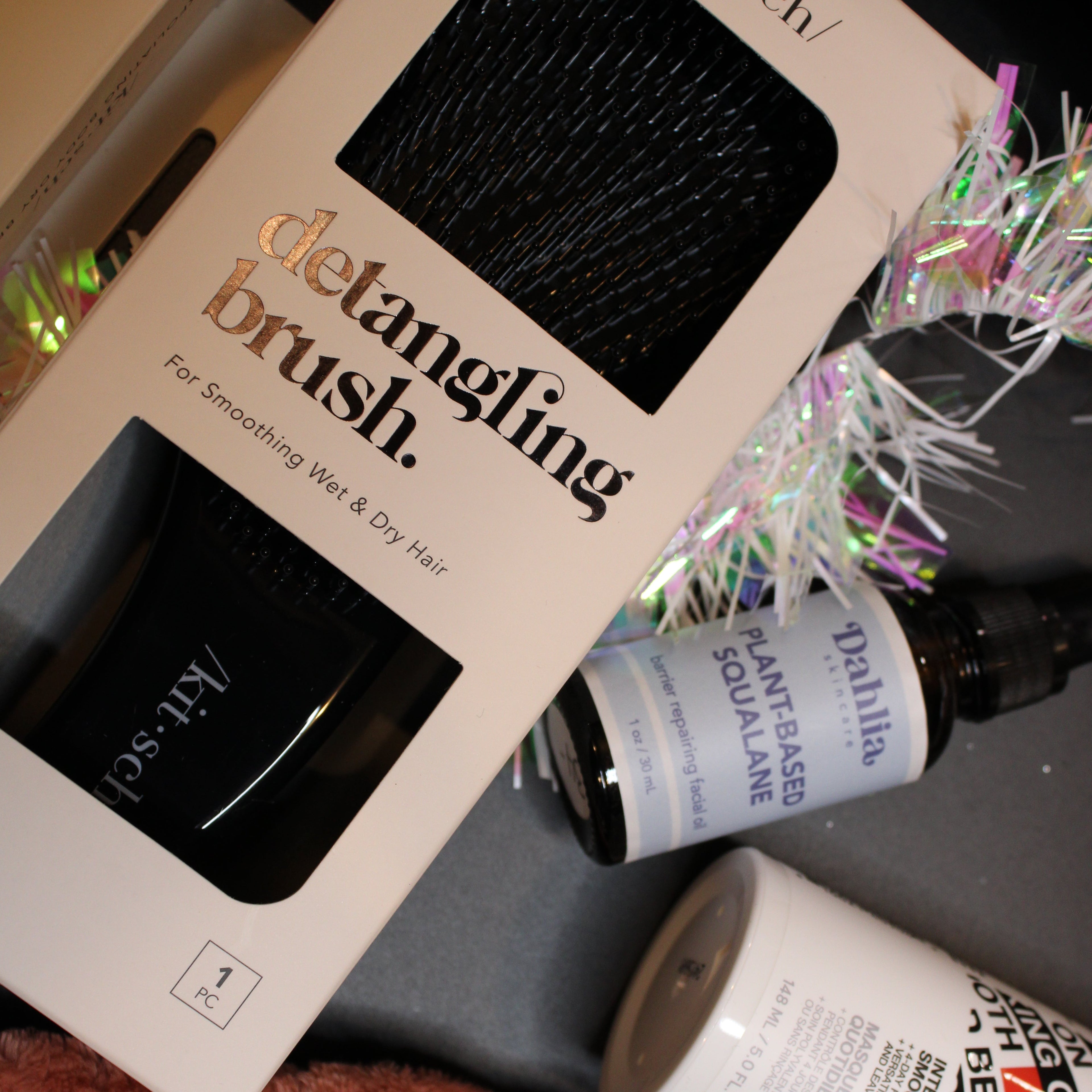 Product display with 'kit selv' detangling brush, 'Dahlia' bottle, and other items on a surface.