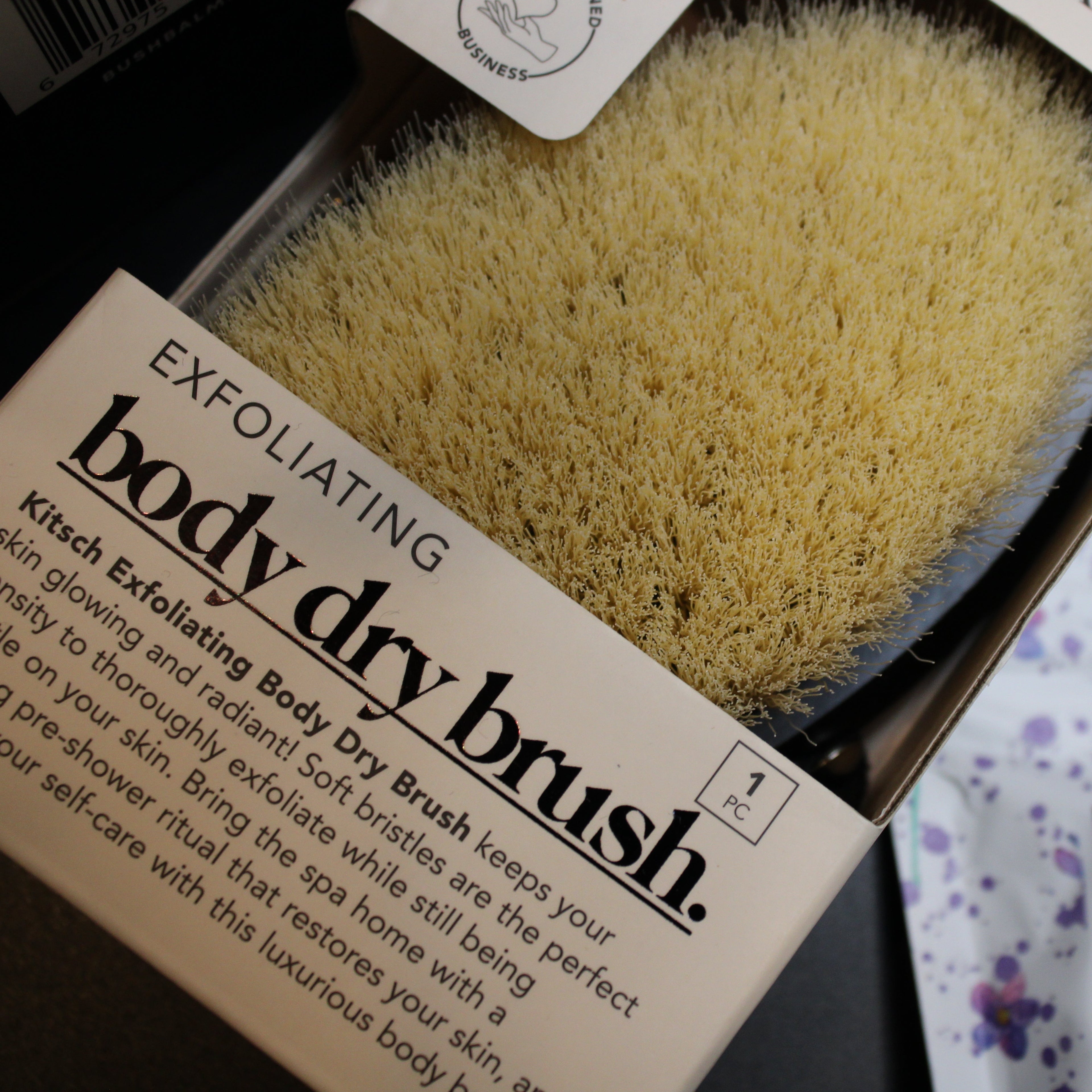 Exfoliating body dry brush in packaging with visible text and a blurred background.