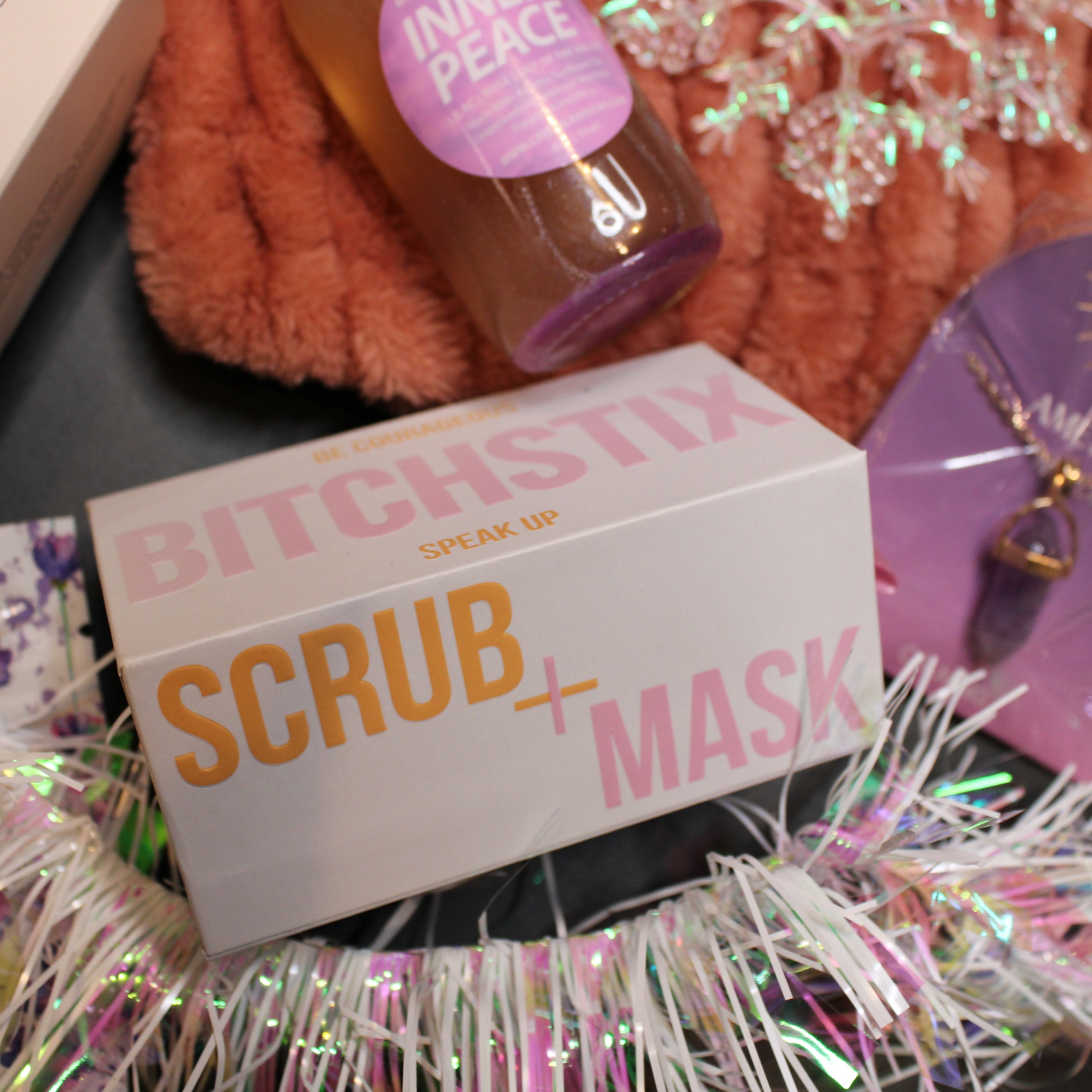 Product packaging with text 'Bitchistix Scrub + Mask' on a decorative background.
