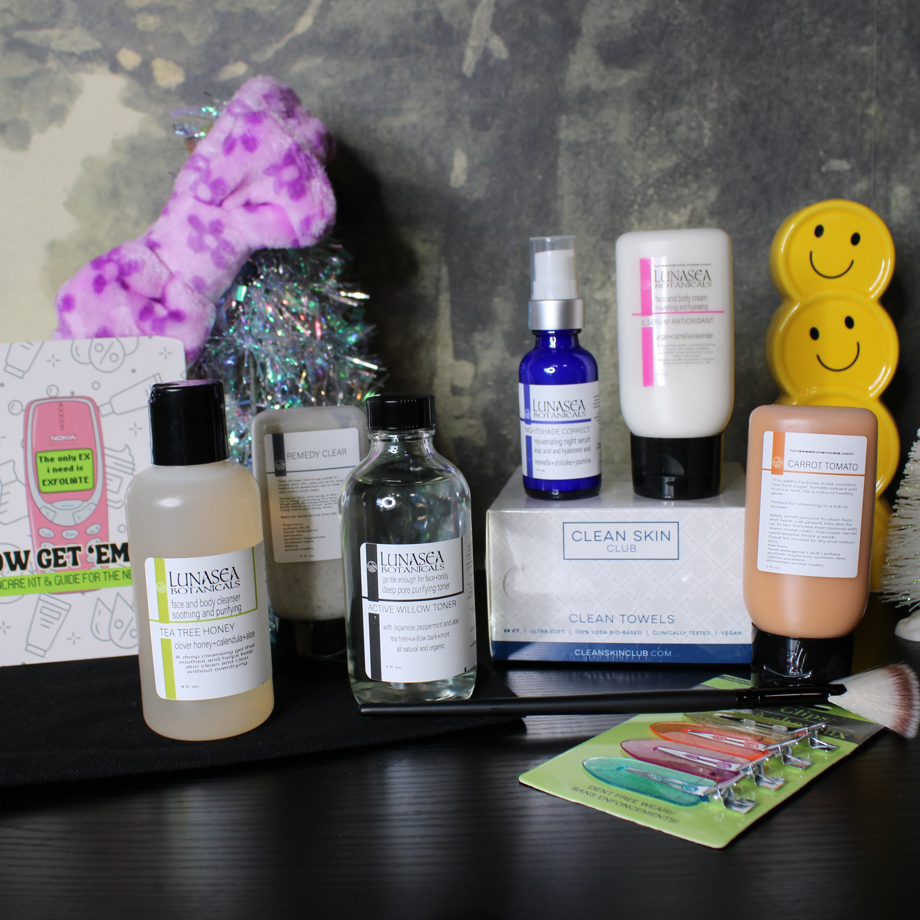 Collection of skincare products and accessories on a dark surface with a textured gray background.